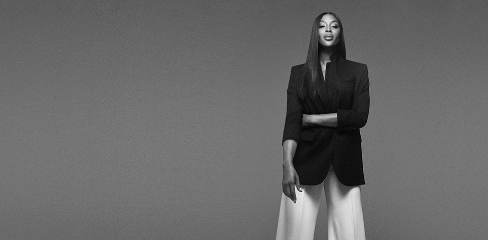 Schwarzweiß Foto von Naomi Campbell mit schwarzem Jacket und weißer, weiter Hose (Foto)