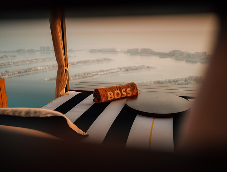 HUGO-BOSS-Handtuch auf einer Liege; im Hintegrund sind das Meer und Gebäude (Foto)